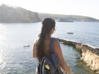 Plajda kayaları olan bir kadın, kristal berrak su koyunda