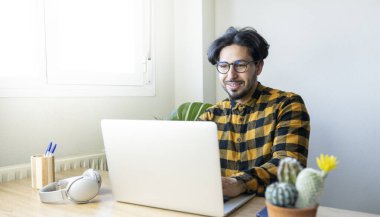 Parlak bir ofiste bilgisayar başında oturan Latin bir adam.