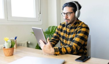 Masada oturan yakışıklı adam kulaklıklı bir tablet kullanıyor.