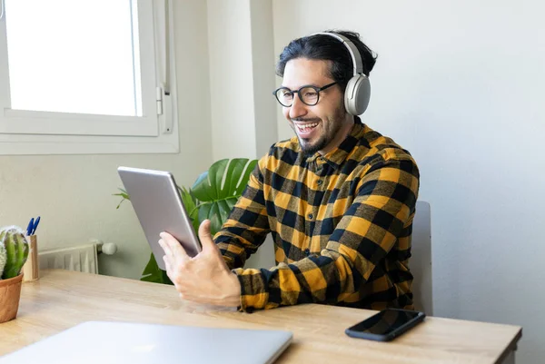 Masada oturan mutlu yakışıklı adam kulaklıklı bir tablet kullanıyor.