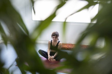 Kadın arka planda yoga yaparken etrafını yapraklar sarıyor.