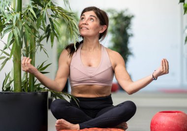 Bitkilerle dolu bir egzersiz odasında pilates yapan mutlu bir kadın.