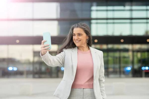 business woman walking through financial city with smartphone, senior woman,