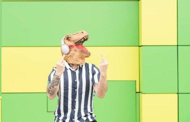 Dinozor maskeli ve kulaklıklı güzel yeşil ve sarı arka planda biri.