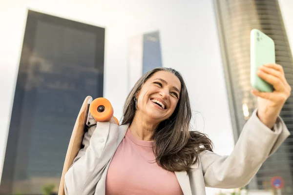 mature business woman is happy with her smartphone and a skateboard in the city