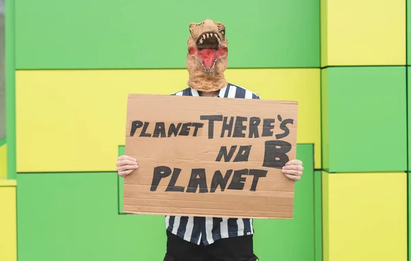 man with a dinosaur mask, with a banner protesting pollution to the planet