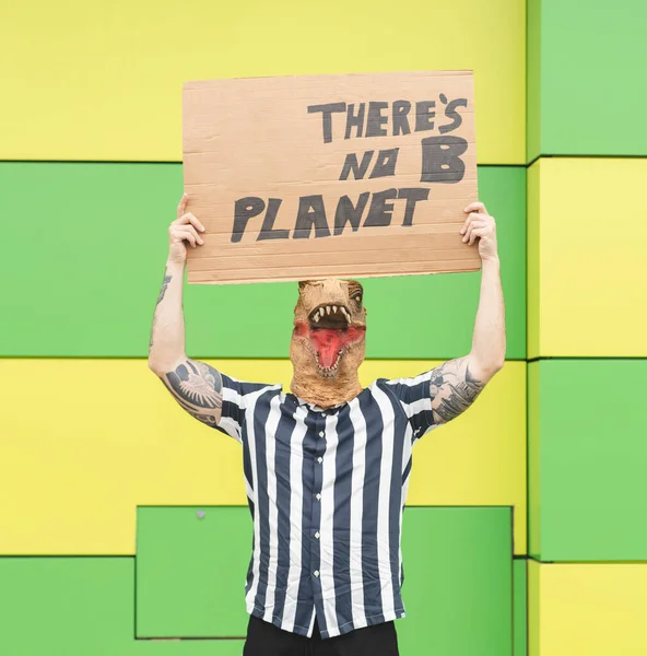 man with a dinosaur mask, with a banner protesting pollution to the planet