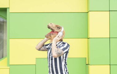 man with dinosaur mask listening to music on green background