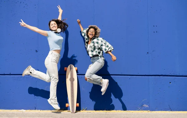Dwie Śmieszne Kobiety Skaczące Razem Niebieskiej Ścianie Słuchające Słuchawek Muzycznych — Zdjęcie stockowe