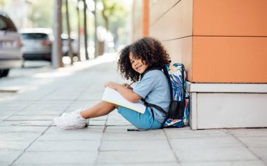 Yakışıklı afro çocuk okuldan sonra ödevlerini yapıyor, yerde oturuyor, anaokuluna gidiyor.