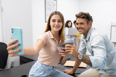 Gülümseyen ofis çalışanları iş yerinde kahve içerken selfie çekiyorlar.