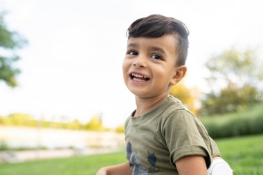 Parkta oturan yakışıklı çocuk kameraya bakıyor.