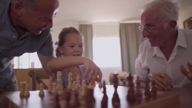 Memlekette satranç tahtası oynayan neşeli çoklu nesil aile. Büyükbaba torununa taktik öğretirken gururlu baba neşeyle gülüyor ve izliyor.