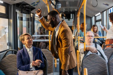 Çeşitli yolcular toplu taşıma otobüsünde konuşurken ve iletişim kurarken, şehirde birlikte seyahat eden çeşitli yaşları ve etnik kökenleri gösteriyor.