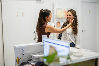 Profesyonel bir klinikte ya da iş yerinde, modern bir resepsiyonda gülümseyen bir müşteriye bilgi ve hizmetle yardım eden arkadaş canlısı bir kadın çalışan.