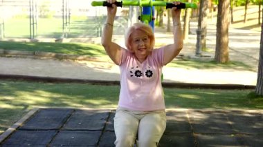 İki neşeli son sınıf öğrencisi parkta güneşli bir günün tadını çıkarıyor. Bir tanesi omuz presi makinesinde egzersiz yaparken arkadaşı sağlıklı ve aktif bir yaşam tarzı için destek ve teşvik sağlıyor.