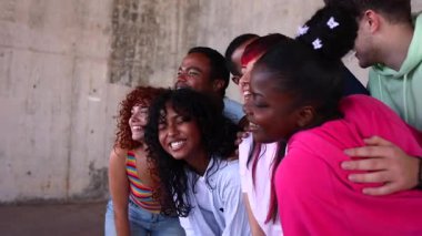 Büyük bir grup mutlu çoklu etnik arkadaş birlikte gülüyor, samimi bir bağ ve arkadaşlığı kucaklıyor ve açık bir şehir ortamında eğlenceli bir anın tadını çıkarıyor.