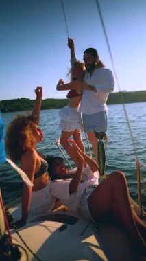 Bir grup çok kültürlü arkadaş, protez bacaklı bir adam, bir yelkenlide canlı bir günbatımı partisinde dans eden, arkadaşlığı, dahil olmayı ve neşeli bir yaz tatilini kutlayan bir adam.