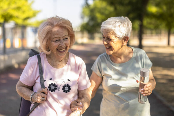 Two cheerful senior women enjoying an active lifestyle, walking together in a park, holding hands, and sharing a happy moment while exercising outdoors