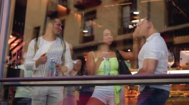 Bir grup mutlu genç arkadaş şehrin modern restoranının tezgahında otururken sosyalleşiyorlar ve yemek yiyorlar. Şehir hayatının yansımaları pencereden görülüyor.