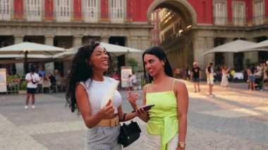 Yaz tatilinin tadını çıkaran iki güzel genç kadın Madrid, İspanya 'daki tarihi plaza belediye başkanında dolaşırken birlikte gülüp akıllı telefon ekranına bakıyorlar.