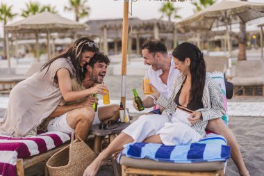 Yaz tatilini ferahlatıcı içeceklerle kutlayan dört mutlu arkadaş, şemsiyenin altında oturup kahkahalarımızı ve iyi zamanlarımızı paylaşan kumsalda uzananlar.