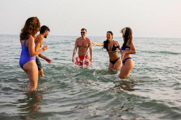 Diverse group of young adult friends swimming and splashing in the ocean, laughing and having fun together during a summer beach holiday, celebrating friendship and joy