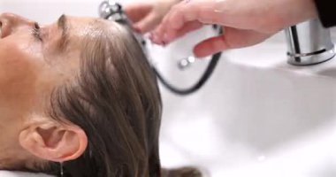 Profesyonel kuaför, yaşlı ve rahat bir kadının saçını kuaförde dikkatlice yıkıyor. Yaşlılar için, beyaz bir arka planda, yetenekli bir kuaför tarafından yapılan güzellik tedavi konsepti.