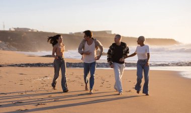 Gün batımında kumlu bir sahilde koşan ve neşeyle yürüyen dört farklı arkadaştan oluşan bir grup. Tatilin, özgürlüğün ve arka planda okyanus dalgaları olan birlikteliğin tadını çıkarıyorlar.