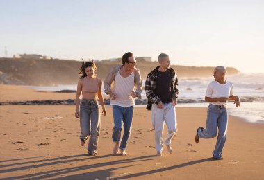 Çeşitli yetişkin arkadaş grupları birlikte aktif zaman geçiriyorlar. Altın saat boyunca kumsalda çıplak ayakla koşuyorlar. Neşe ve özgürlüğü yansıtıyorlar.