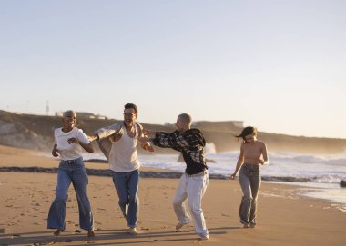 Günbatımında okyanus kıyısında çıplak ayakla koşan çeşitli yetişkin arkadaş grupları yaz tatili boyunca özgürlük, mutluluk ve arkadaşlığın tadını çıkarıyorlar.