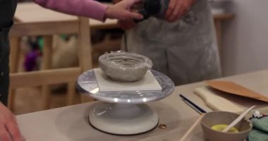 Çömlek atölyesinde küçük bir kase üzerinde çalışan bir zanaatkârla bir öğrencinin elleri. Öğretmen, kadının yeni seramik sanat eserinden koruyucu filmi çıkarmasına yardım eder.