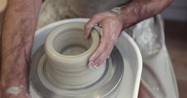 Sanatçının elleri, dönen bir çömlek çarkının üzerindeki ıslak çamuru profesyonelce şekillendiriyor, atölyede seramik bir kap veya vazo ustalıkla hazırlıyor, el yapımı geleneksel çömlek sürecini gözler önüne seriyor.