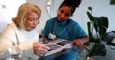 Üst düzey bir kadın bakıcısıyla aynı masada oturuyor, bir fotoğraf albümündeki eski resimlere bakıyor, bir ev bakımı ziyareti sırasında geçmişten anıları anlatıyor.