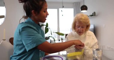 Yaşlı bir kadına günlük ilaçlarını haftalık bir organizatörden almasında yardım etmek, bir ev sağlık hizmeti ziyareti sırasında bir bardak su ve destek sağlamak.