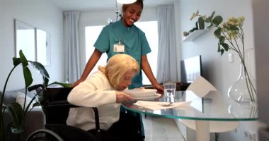 - Genç. Gülümseyen kadın bakıcı tekerlekli sandalyedeki yaşlı bir kadına yardım ediyor. Modern bir dairede, yemek masasına bir tabak yemek götürmek. Ev bakımı yardımı ve arkadaşlık.