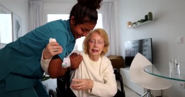 Neşeli bir sağlık görevlisi, son sınıf bir kadına hareket kabiliyeti olan yardım ediyor, ev ziyareti sırasında tekerlekli sandalyeden kalkması ve fizik tedavi ve şefkat göstermesi için ona destek oluyor.