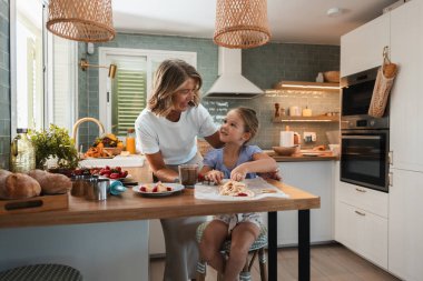 Büyükanne ve torun, parlak, modern bir mutfakta birlikte tatlı pişirirken gülümsüyor, kahkahalar atıyor, öğretmenlik yapıyor ve nesillerarası bağ kuruyor.