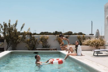 Üç kişilik bir aile, güneşli bir havuza atlıyor, rengarenk bir yüzme ringiyle, ebeveynler ve kızlar kaygısız bir yaz tatilinde gülüyor ve kaynaşıyorlar.