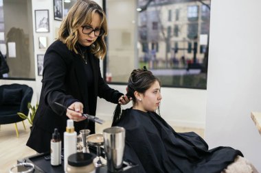 Kuaför, genç bir müşterinin saçını boyama işlemi için kırpılmış bölümlerle hazırlıyor. Modern bir kuaför salonunda çalışırken elinde fırça tutuyor.