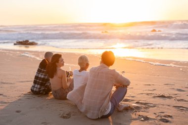 Genç arkadaşlar kumlu bir sahilde altın saatinde dinleniyorlar, güneşin okyanusun üzerinde batışını izliyorlar, ılık, huzurlu beraberlik anlarını ve yaz kaçışını paylaşıyorlar.