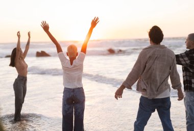 Neşe ve özgürlüğü ifade eden çeşitli genç yetişkinler bir kumsalda büyüyen, okyanusun üzerinde sakin günbatımında yaşamı ve bağlantıyı kutlayan