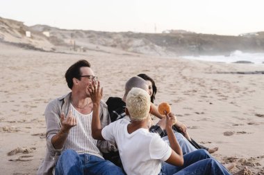 Günbatımında okyanusun kıyısındaki eğlenceli ve sıradan bir toplantının keyfini çıkaran farklı genç arkadaşlar, kahkahalarla ve kaygısız bir sosyal ortamda pozitif duygularla bağlanıyorlar.