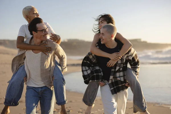 Altın saat boyunca kumlu bir sahilde birbirini sırtında taşıyan iki neşeli genç çift, okyanusun kıyısındaki neşe, dostluk ve kaygısız yaz anlarını somutlaştırıyor.