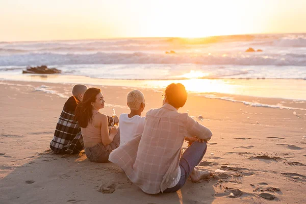 Genç arkadaşlar kumlu bir sahilde altın saatinde dinleniyorlar, güneşin okyanusun üzerinde batışını izliyorlar, ılık, huzurlu beraberlik anlarını ve yaz kaçışını paylaşıyorlar.