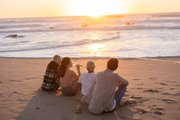 Bir grup genç arkadaş kumlu bir plajda oturup güzel okyanus günbatımını seyrediyor ve yaz akşamları birlikte sıradan bir içki içiyorlar.