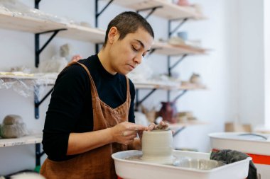 Parlak bir stüdyo ortamında el işçiliğinin yaratıcı sürecine odaklanarak seramik bir kap üzerinde ustalıkla ıslak çamuru şekillendirip seramik bir kap haline getirmek.