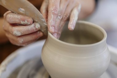 Zanaatkârın becerikli elleri, seramik bir kap şeklini çömlek tekerindeki ıslak çamurdan alıyor. Bu da geleneksel el sanatları sürecini ve bir stüdyo ortamında sanatsal yaratımı gösteriyor.