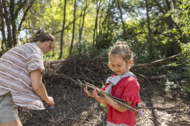 Anne ve kızı güneşli bir ormanda çubuk topluyor, doğayı, keşfi ve sıcak bir bahar gününde açık havada oynamayı öğrenirken kaynaşıyorlar.
