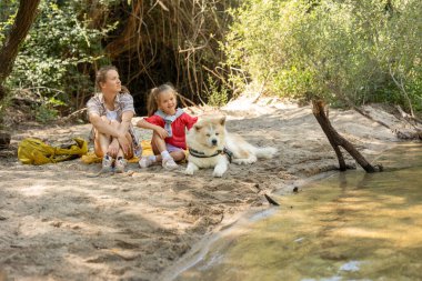 Aile kumlu bir nehir kıyısında doğanın tadını çıkarıyor, büyük yoldaşlarıyla birlikte denize bakıyor, yaz gezintisi sırasında huzurlu bir açık hava anının tadını çıkarıyor.